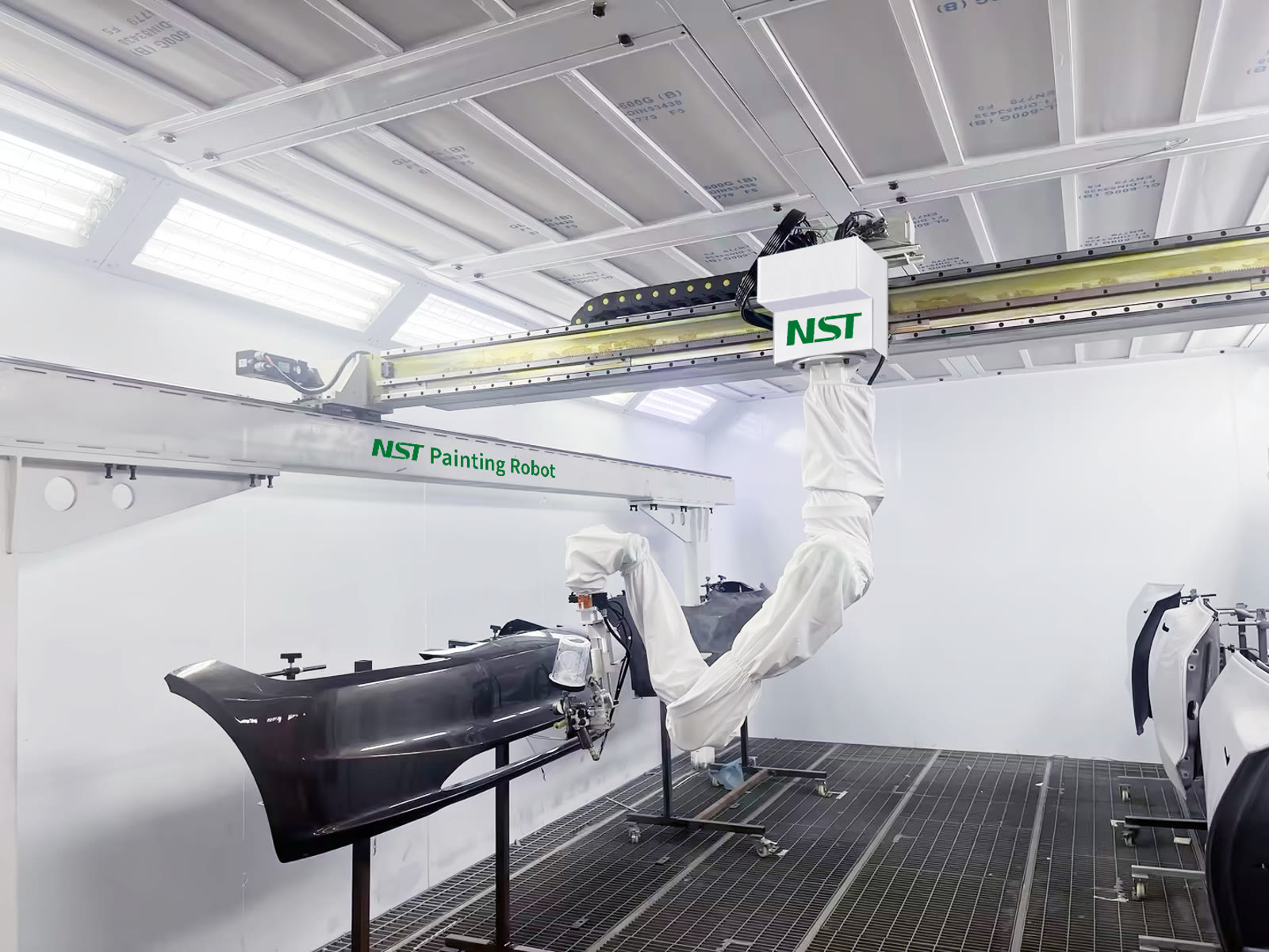 The NST robot spraying a black bumper while door panels wait on stands in the same booth cycle